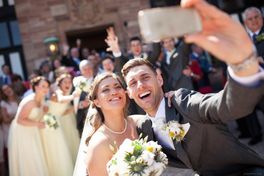 A-young-bride-and-groom-take-a-selfie-in-front-of-their-wedding-guests
